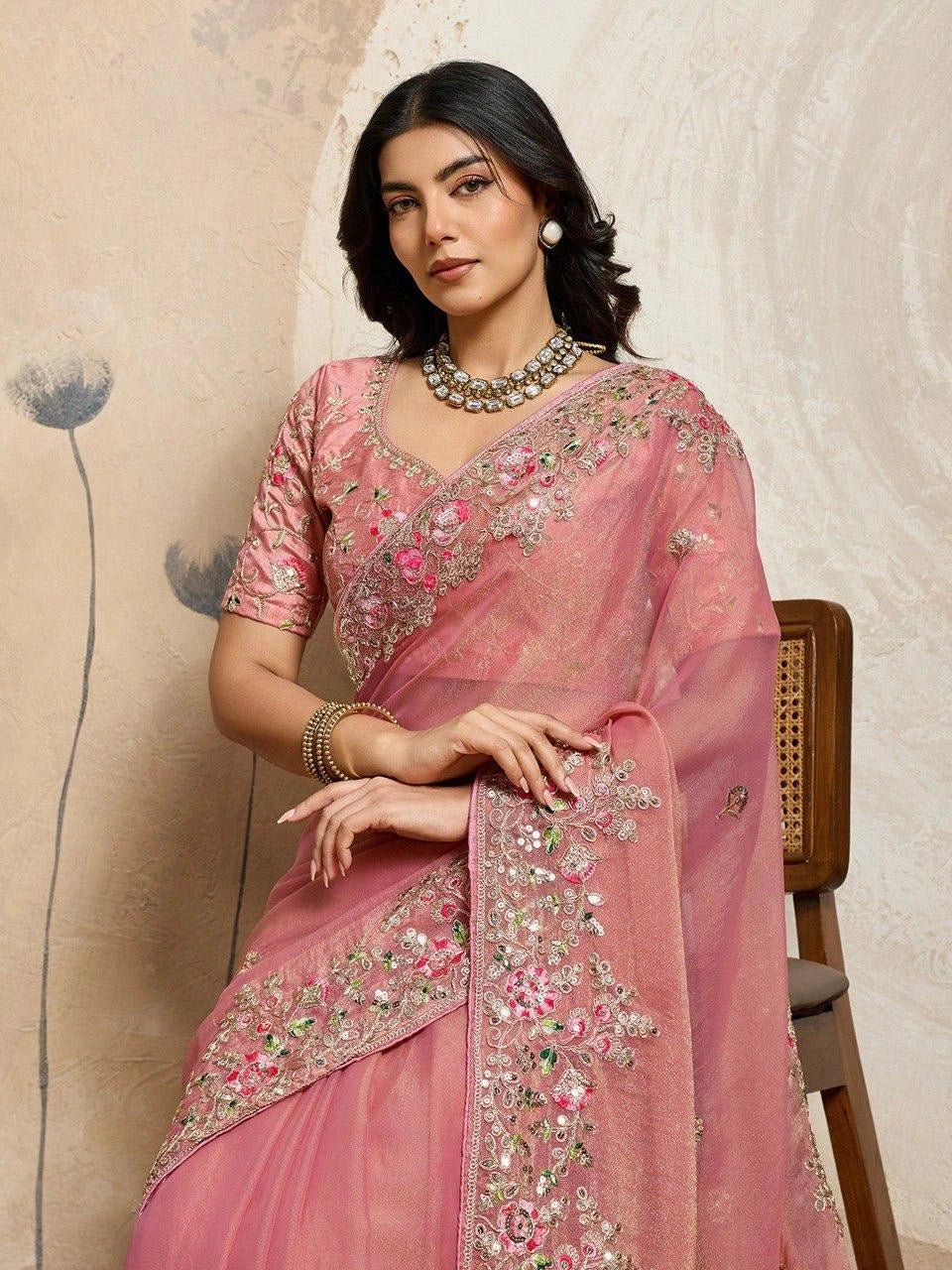 Woman wearing a pink saree with intricate designs against a beige background
